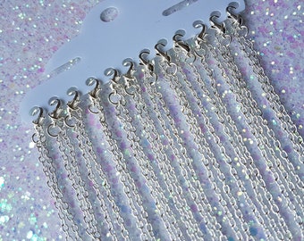 May include: A pack of 12 silver chain necklaces with lobster claw clasps. The chains are displayed on a white card with a hanging hole.