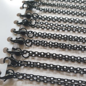 May include: A set of ten black metal chains with lobster claw clasps. The chains are displayed on a white card.