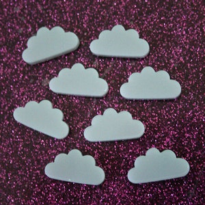 May include: Eight white cloud-shaped embellishments on a pink glitter background.