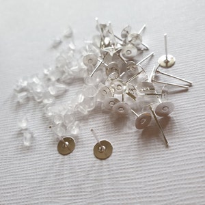 May include: A pile of silver earring posts with clear rubber earring backs.