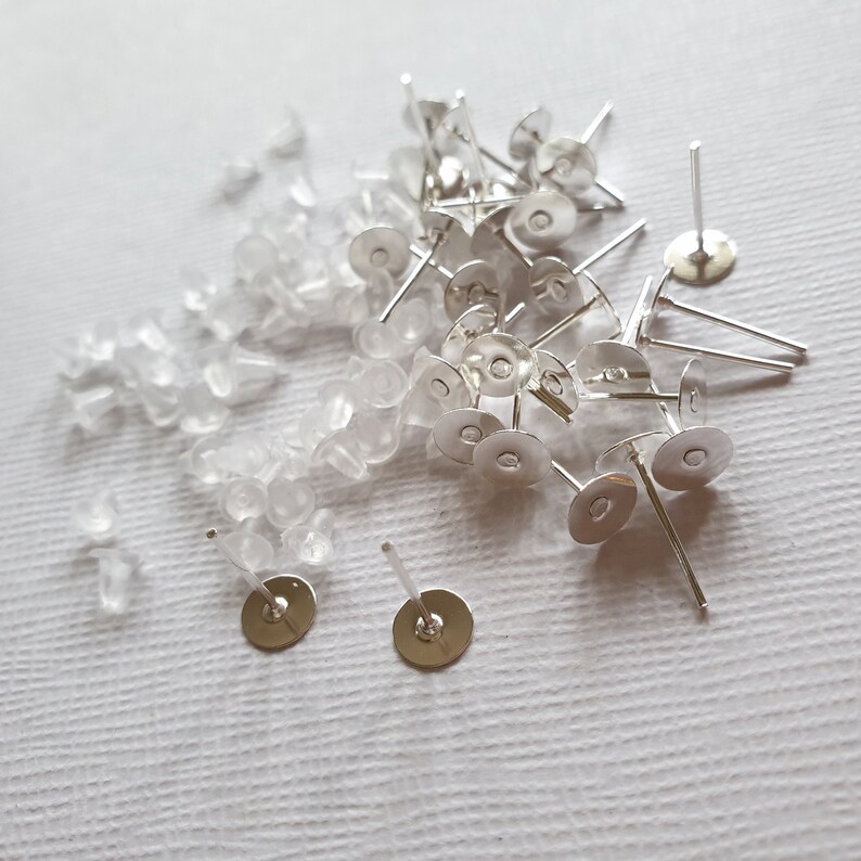 May include: A pile of silver earring posts with clear rubber earring backs.