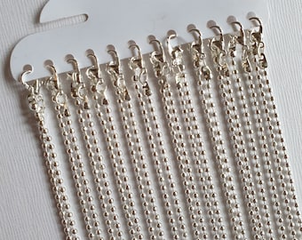 May include: A pack of 15 silver ball chain necklaces, each with a lobster clasp. The chains are hanging from a white plastic card with a hole at the top for hanging.