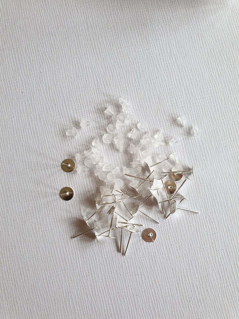 May include: A pile of clear plastic earring backs and silver earring posts on a white surface.