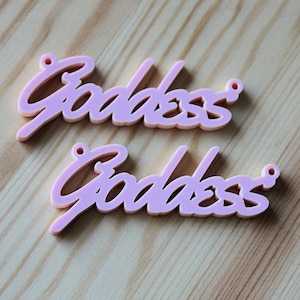 May include: Two pink acrylic charms with the word "Goddess" written in a cursive font.