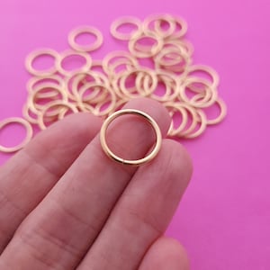 May include: A pile of gold jump rings, with one ring held in a hand. The jump rings are small and round, and they are perfect for jewelry making.