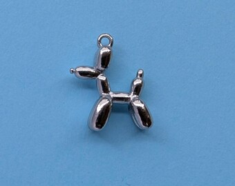 May include: A silver-colored charm in the shape of a balloon dog. The charm has a loop at the top for attaching to a necklace or bracelet. The dog is depicted in a playful pose, with its body and limbs formed by rounded shapes.
