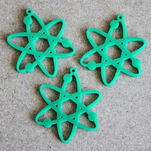 May include: Three bright green, flat, star-shaped charms with a central hexagonal cutout and circular accents at each point. Each charm features a small hole at the top for attachment, displaying a consistent atomic-inspired geometric design.