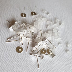 May include: A pile of silver earring posts and backs, with clear plastic earring backs scattered around them.