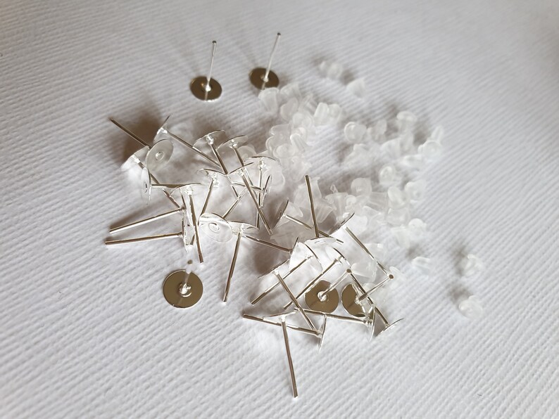 May include: A pile of silver earring posts and backs, with clear plastic earring backs scattered around them.