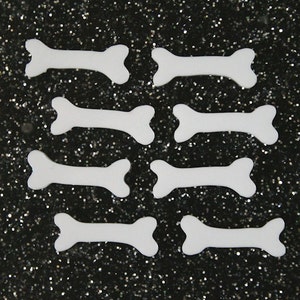 May include: Eight white foam bone shapes on a black glitter background.