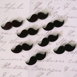 May include: Eight black felt moustache shapes on a white background with handwritten text.