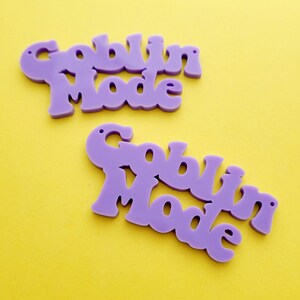 May include: Two purple acrylic ornaments with the text "Goblin Mode" in a whimsical font.