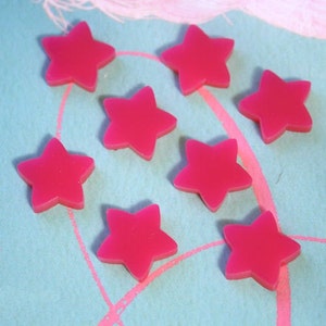 May include: Eight pink star-shaped candy pieces on a blue background.