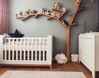 Puede incluir: Un cuarto de niños con una cuna blanca, una estantería de madera con forma de árbol que contiene animales de peluche y una cómoda blanca. La habitación tiene una paleta de colores neutros con una pared gris y una alfombra de color claro.
