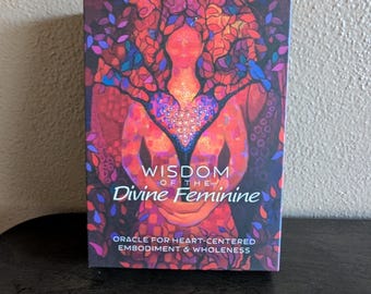 May include: A rectangular oracle card deck box featuring a vibrant illustration of a figure with a heart-shaped chest and tree-like branches. The text reads WISDOM OF THE Divine Feminine ORACLE FOR HEART-CENTERED EMBODIMENT & WHOLENESS in white.