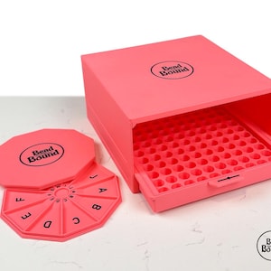 Pode incluir: Uma caixa rosa para guardar contas com uma bandeja retrátil e uma tampa. A tampa e uma bandeja de classificação separada são visíveis. A caixa e a tampa têm a inscrição "Bead Bound" em preto.