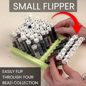 Peut inclure: Un organiseur de perles vert clair, intitulé "Small Flipper", contenant de nombreux tubes transparents remplis de perles. Le texte "EASILY FLIP THROUGH YOUR BEAD COLLECTION" est également visible. L'organisateur est en cours de basculement.