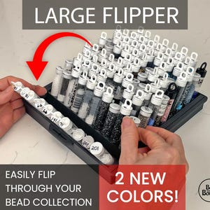 May include: A black bead storage container labeled "LARGE FLIPPER" filled with numerous small, clear tubes. Each tube contains beads of various colors and textures. The image includes the text "EASILY FLIP THROUGH YOUR BEAD COLLECTION" and "2 NEW COLORS!"