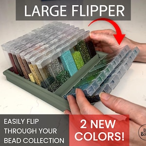 Puede incluir: Un organizador de cuentas verde, etiquetado como "LARGE FLIPPER", con compartimentos transparentes y con bisagras. Los compartimentos están llenos de cuentas de varios colores, incluyendo rojo, dorado, verde y azul. El texto dice "EASILY FLIP THROUGH YOUR BEAD COLLECTION" y "2 NEW COLORS!"