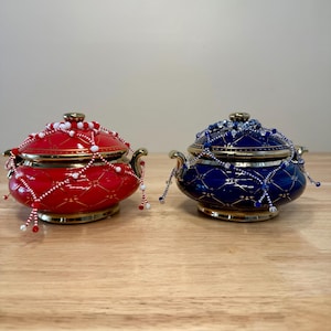 May include: Two ceramic serving dishes with lids, one red and one blue, decorated with gold trim and white and blue beads.