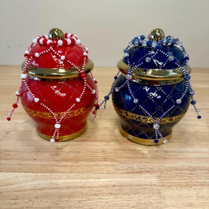 May include: Two decorative ceramic jars with gold trim and beaded accents. One jar is red with white beads and the other is blue with clear beads.