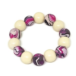 May include: A bracelet made of wooden beads with a pink, white and black marbled pattern. The bracelet is made of 12 beads, alternating between plain white and marbled.