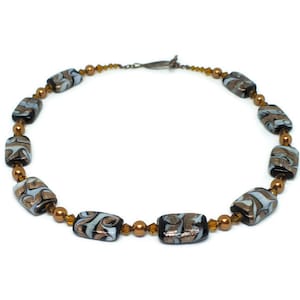 May include: A gold and black necklace with rectangular glass beads featuring a swirling pattern. The beads are separated by small gold beads.