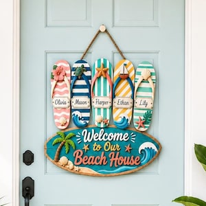 Op de afbeelding: Een decoratief houten wandbord met vijf kleurrijke slippers met de namen Olivia, Mason, Harper, Ethan en Lily, hangend boven een ovaal bord met de tekst Welcome to Our Beach House en een afbeelding van een palmboom en een golf.
