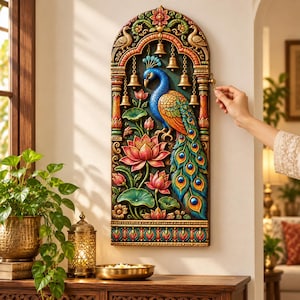 May include: A rectangular wall hanging featuring a relief carving of a blue and orange peacock surrounded by pink lotus flowers and green lily pads. The arched frame includes hanging brass-colored bells and decorative bird motifs in gold and red.