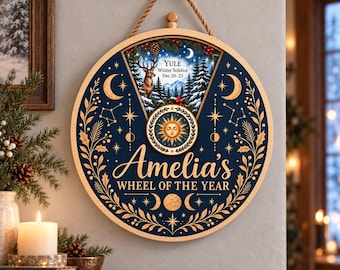 Könnte beinhalten: Ein kreisförmiger Wandbehang aus Holz mit der Aufschrift Amelia's Wheel of the Year. Die dunkelblaue Oberfläche zeigt goldene Himmelsmotive wie Monde und Sterne, ein zentrales Sonnenemblem und einen dreieckigen oberen Bereich mit Winterwald.