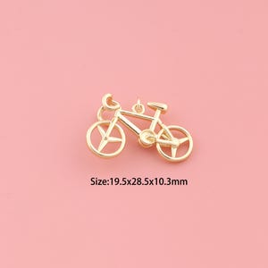 May include: A gold-colored bicycle charm with a loop for hanging. The bicycle has a classic design with a seat, handlebars, and wheels. The charm measures 19.5mm x 28.5mm x 10.3mm.