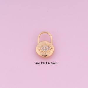 May include: Gold-toned charm with a round evil eye design featuring clear rhinestones. The charm is shaped like a padlock and measures 19x13x3mm.