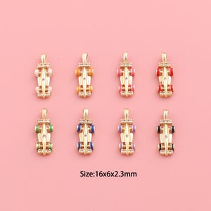 May include: Eight gold-colored charm pendants shaped like race cars, each with colorful enamel accents. The cars have wheels in various colors, including white, orange, pink, red, green, blue, purple, and black. Each charm measures 16x6x2.3mm.