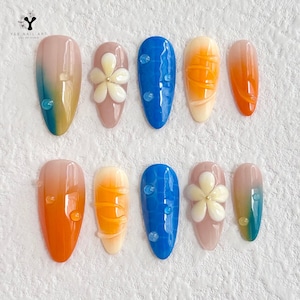 Puede incluir: Diez uñas postizas con diferentes diseños. Los diseños incluyen un degradado azul con una flor blanca, un degradado amarillo con una flor blanca, un degradado azul con una flor blanca, un degradado amarillo con una flor blanca, un degradado azul con una flor blanca, un degradado amarillo con una flor blanca, un degradado azul con una flor blanca, un degradado amarillo con una flor blanca, un degradado azul con una flor blanca y un degradado amarillo con una flor blanca.