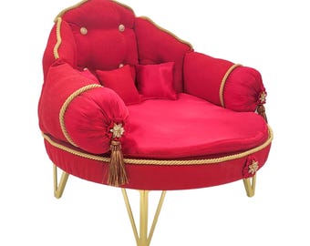 Può includere: Una lussuosa chaise longue rotonda rossa con dettagli dorati. La chaise longue presenta finiture dorate, nappe e gambe dorate. Include due piccoli cuscini quadrati e due cuscini a rullo. Lo schienale ha dettagli con bottoni.
