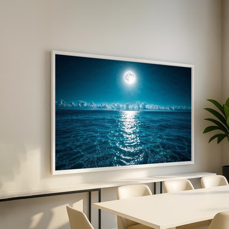 May include: A framed print of a moonlit ocean scene. The image features a bright full moon in a dark blue sky, reflecting a shimmering path of light on the water. White clouds line the horizon, and the water's surface is a deep blue.