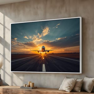 May include: A framed canvas print featuring an airplane taking off at sunset. The image shows the plane centered on the runway, with the sun setting behind it, casting a warm glow. The sky is a mix of orange, yellow, and blue.