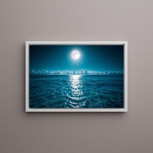 May include: A framed print of a moonlit ocean scene. The image features a full moon shining brightly above the water, with its reflection creating a shimmering path across the dark blue sea. White clouds are visible on the horizon.
