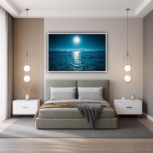 May include: A bedroom with a large framed print of a moonlit ocean scene above a gray bed. The room features white nightstands, decorative hanging lights, and a gray rug. The bed has decorative pillows and a gray blanket.