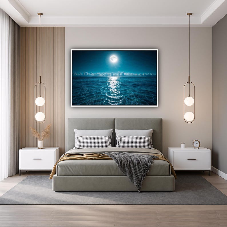May include: A bedroom with a large framed print of a moonlit ocean scene above a gray bed. The room features white nightstands, decorative hanging lights, and a gray rug. The bed has decorative pillows and a gray blanket.