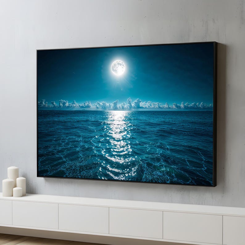 May include: A framed wall art print depicting a moonlit ocean scene. The image features a bright full moon in a dark blue sky, reflecting a shimmering path of light on the water. White clouds are visible along the horizon.