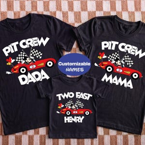 May include: Three black t-shirts with racing-themed graphics. The shirts feature a red race car with Mickey Mouse, checkered flags, and the words "PIT CREW DADA", "PIT CREW MAMA", and "TWO FAST HENRY".