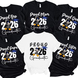 Peut inclure: Plusieurs t-shirts noirs et blancs avec des motifs sur le thème de la remise de diplômes. Chaque chemise porte l'inscription "Proud Bro", "Proud Mom", "Proud Dad", "Proud Papa" ou "Proud Sister" au-dessus du chiffre "26" et du mot "Graduate". Un personnage de dessin animé est également inclus.