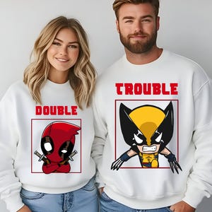 May include: White sweatshirts with a cartoon graphic of Deadpool and Wolverine. The text "Double Trouble" is printed on the sweatshirts.