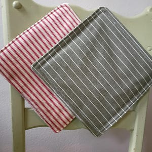 May include: Two square fabric pot holders with striped patterns. One has red and white stripes, the other has gray and white stripes. The pot holders are resting on a light green chair.