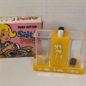 May include: Vintage salt and pepper shaker set with a box. The box is pink with a cartoon woman and the words "Salt' Pepper" and "Push Button". The shaker is yellow with palm tree graphics and the words "Daytona Beach, Florida".