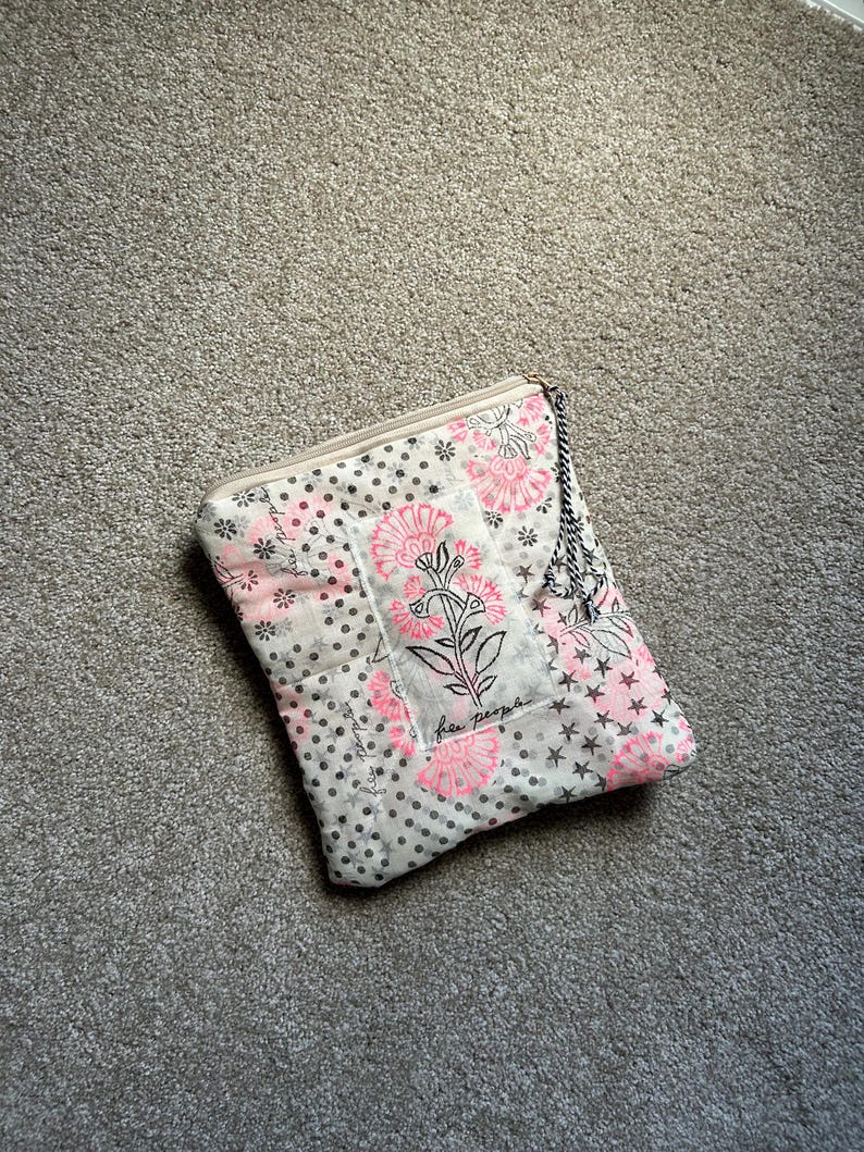 May include: A quilted clutch with a floral pattern in pink and white, accented with black polka dots and stars. The text "free people" is visible. The clutch has a zipper closure and a black and white rope handle.