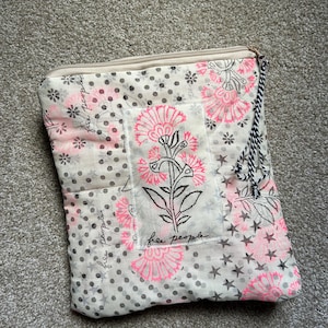 May include: A beige and pink floral patterned pouch with a zipper closure. The pouch features a floral design with the text "free people". The pouch has a black and white tassel attached to the zipper.