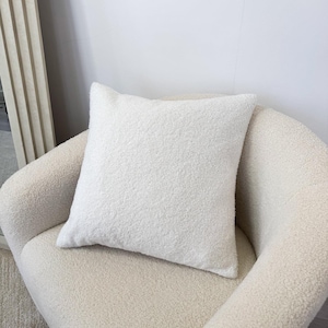 May include: A white fluffy throw pillow on a cream coloured armchair.
