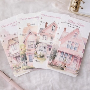 Puede incluir: Cuatro tarjetas con ilustraciones de acuarela de casas rosas. Cada tarjeta presenta un diseño de casa diferente y texto. Las tarjetas están dispuestas sobre una superficie blanca con un bolígrafo, una rosa y cristales.